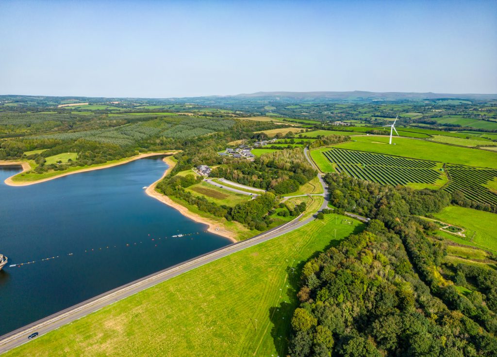 Roadford Reservoir with a solar farm in the foreground and a wind turbine nearby.